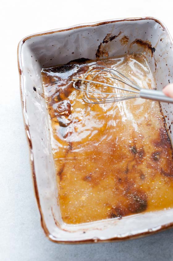 browned bits from the bottom of a baking dish are being scraped with a whisk