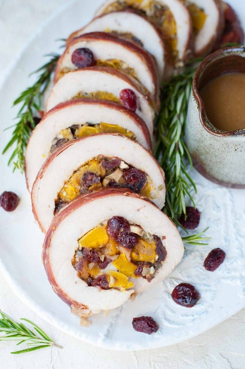 close up photo of turkey roulade with pumpkin and cranberries, rosemary and gravy on the side