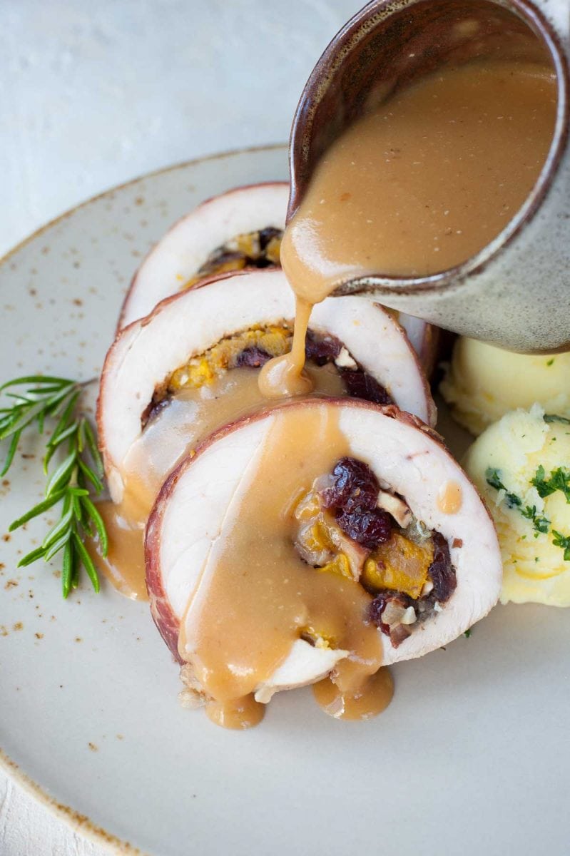 Gravy is being poured over a turkey roulade with butternut squash, mushroom and cranberry stuffing.