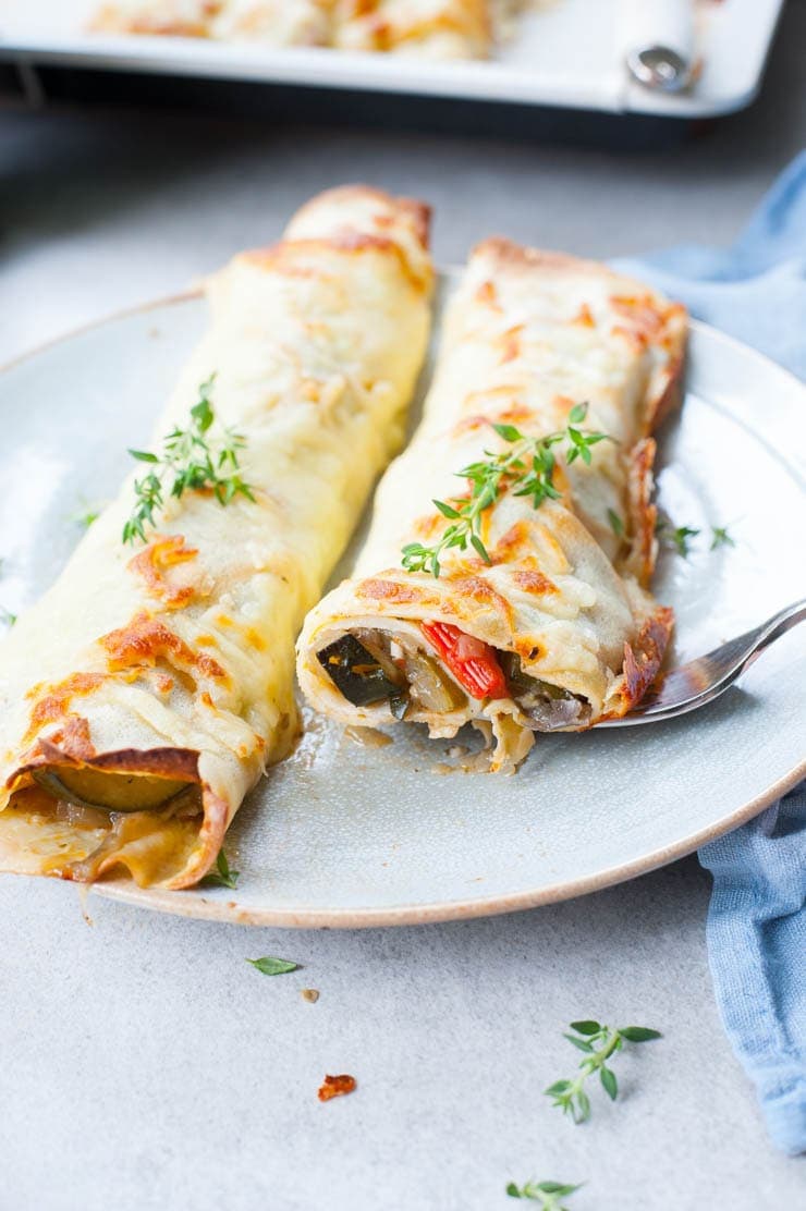Cheesy vegetable crepes cut in half on a blue plate.