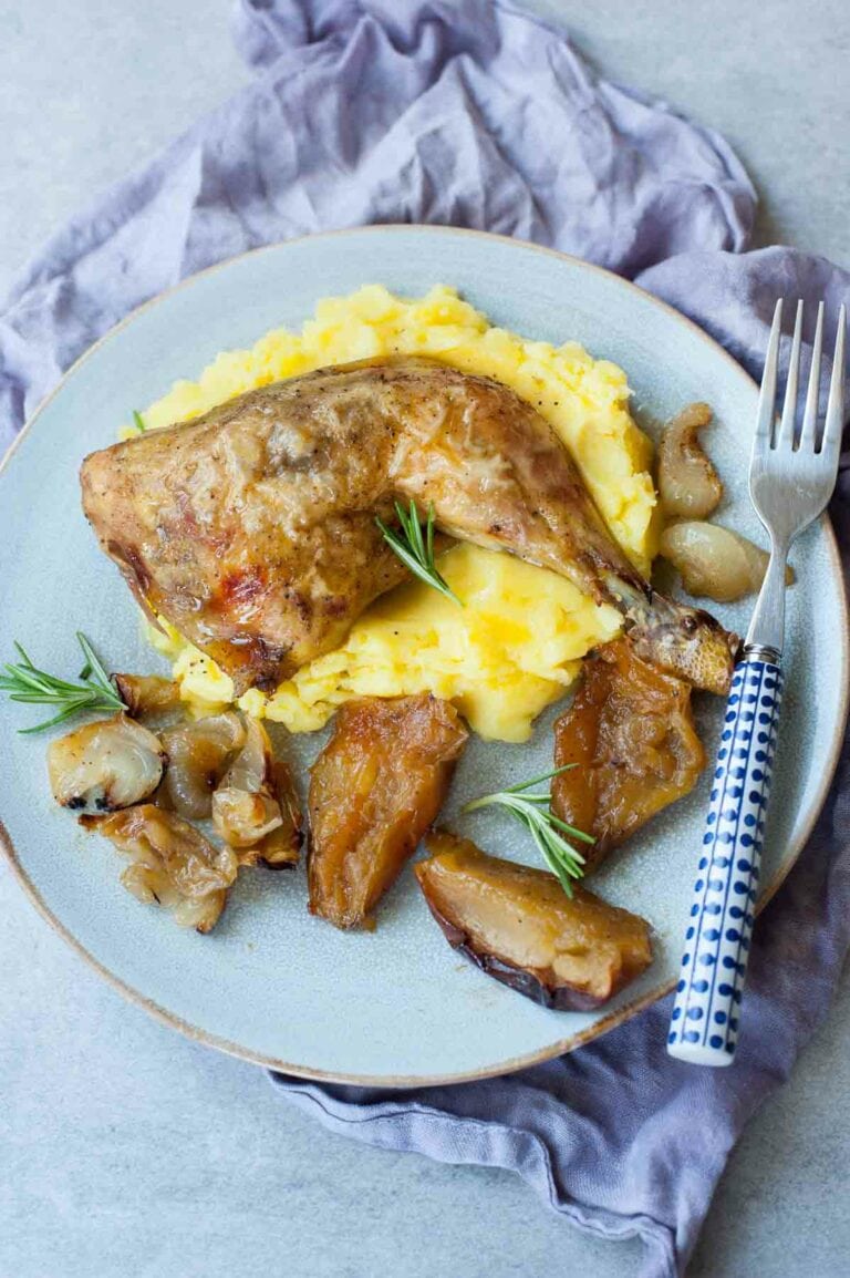 Roasted chicken leg with scrambled eggs and roasted potatoes, garnished with rosemary on white plate.