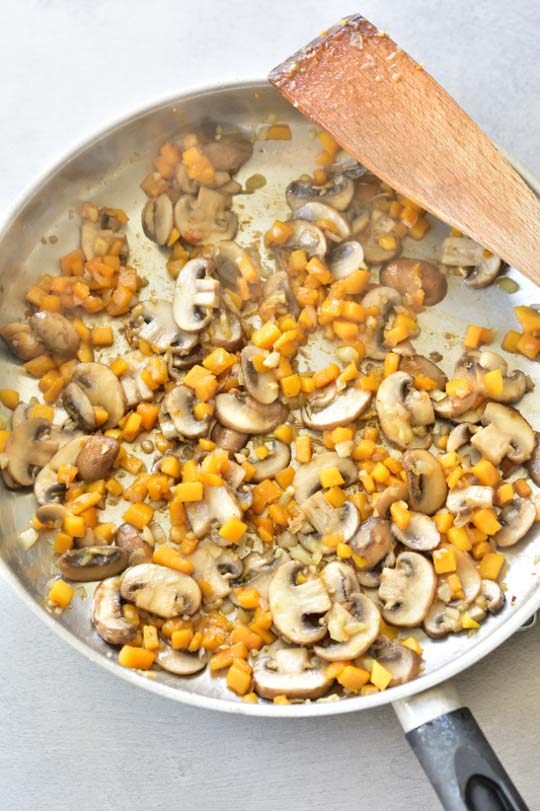 mushrooms and butternut squash are being cooked in a pan
