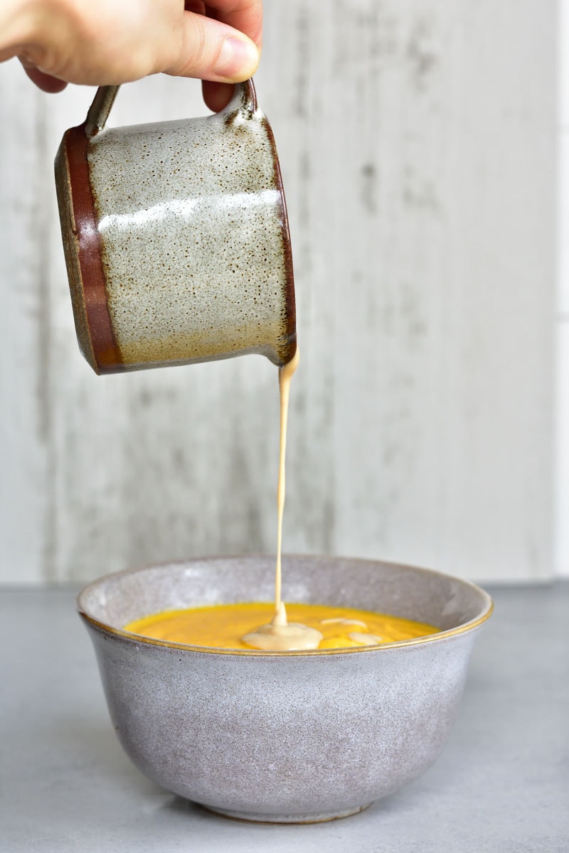 peanut butter sauce is being poured over carrot coconut soup