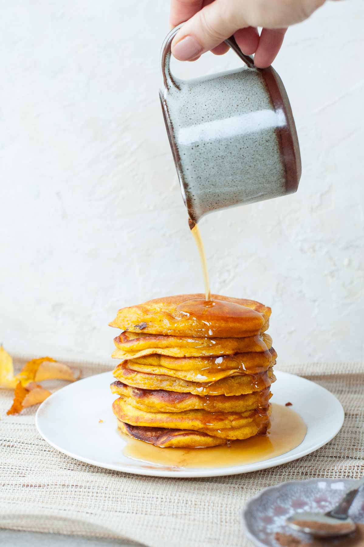 Maple syrup is being poured over a pumpkin pancakes stack.