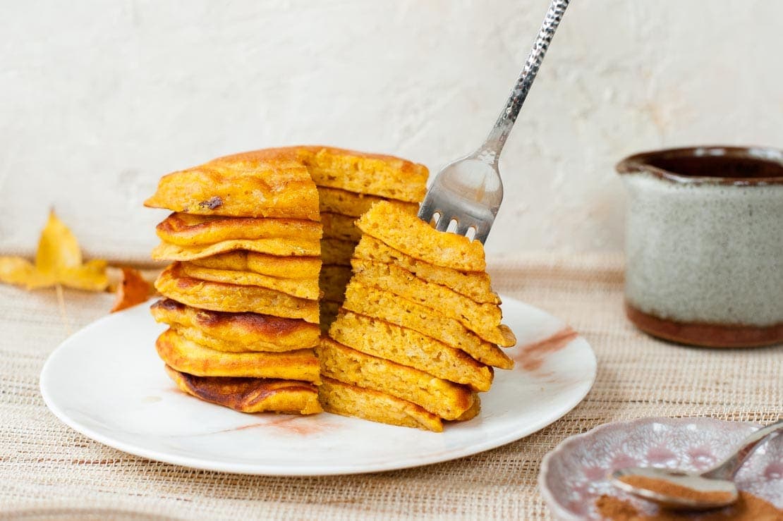 A stack of pumpkin pancakes with a quarter stuck on a fork.