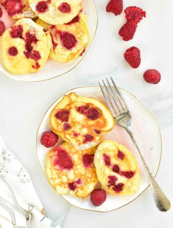 Lemon ricotta pancakes with raspberries on a rose plate.