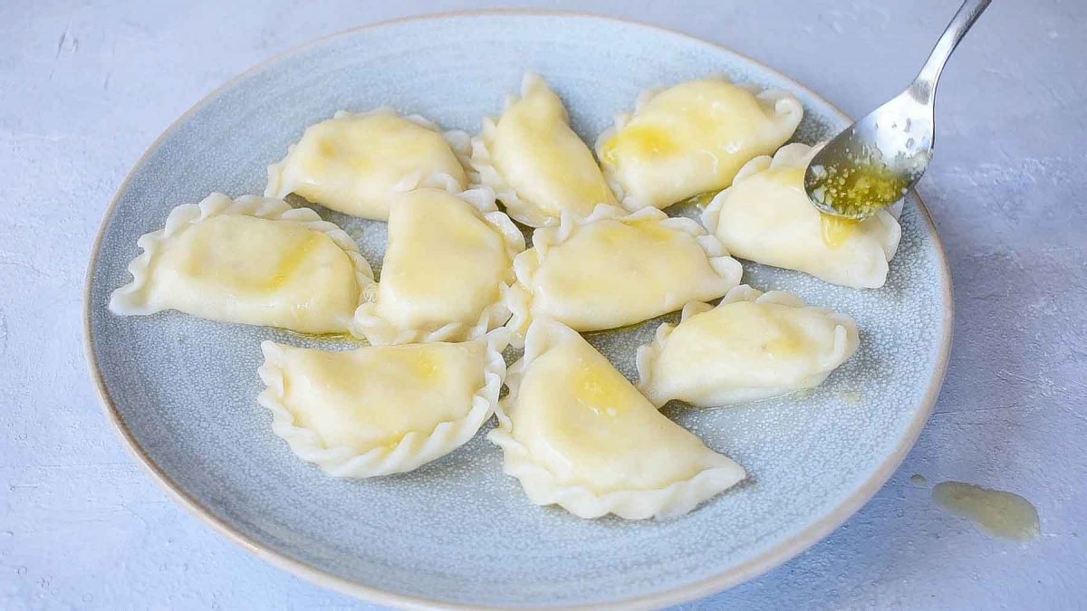 Butter is being poured over pierogi on a blue plate.