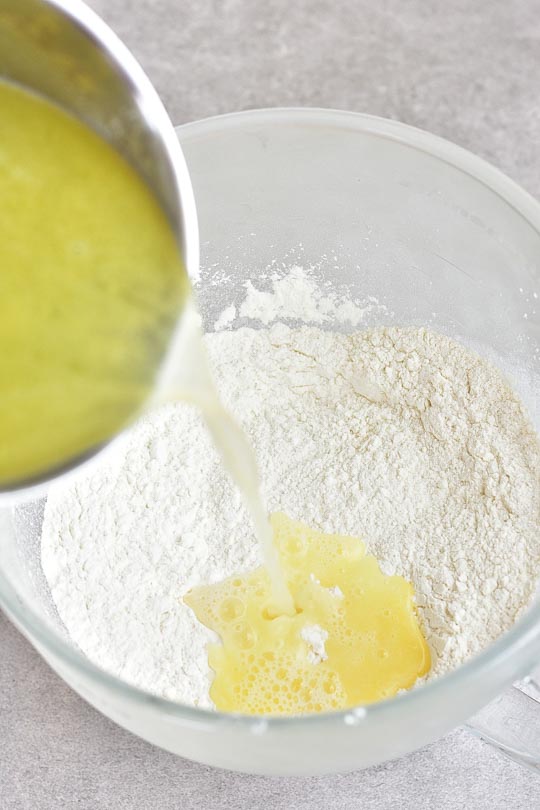 hot water with butter is being poured into a bowl with flour