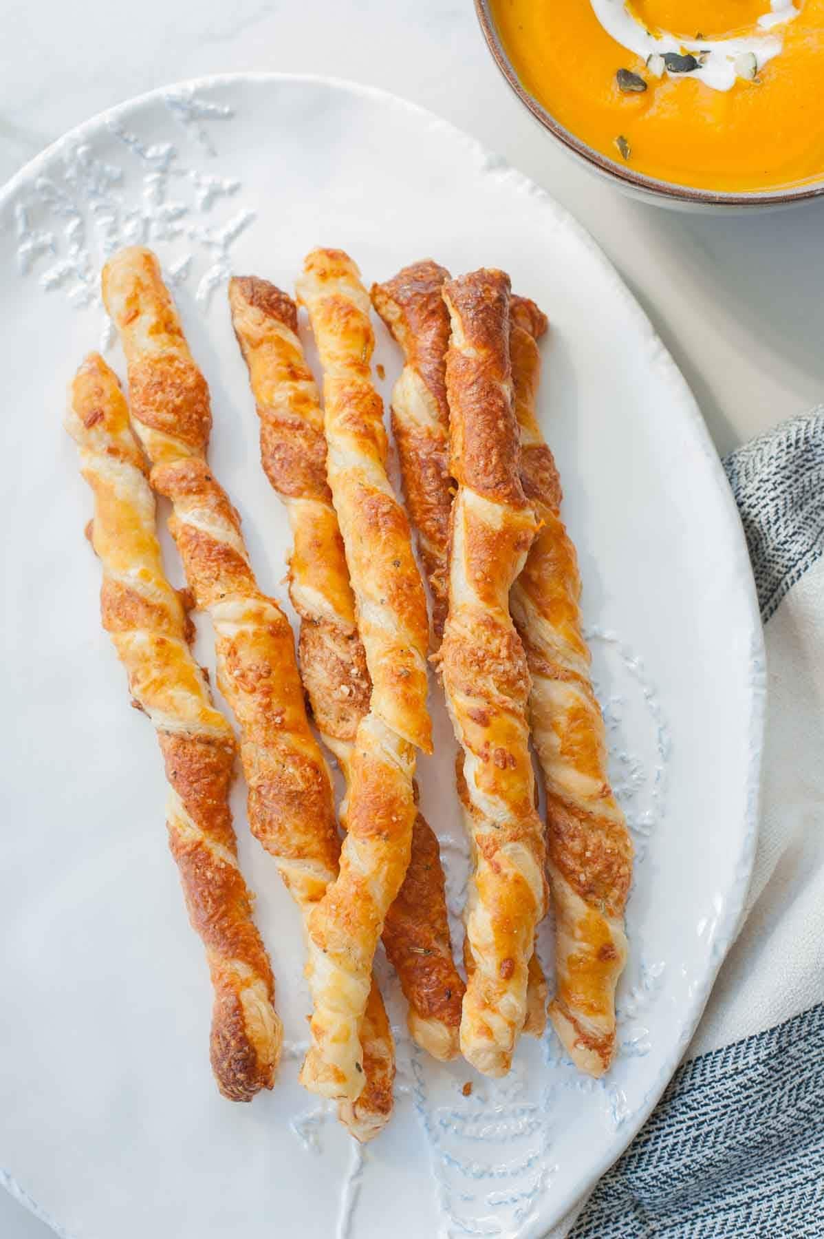 Puff pastry cheese straws on a plate, a bowl of pumpkin soup on the side.