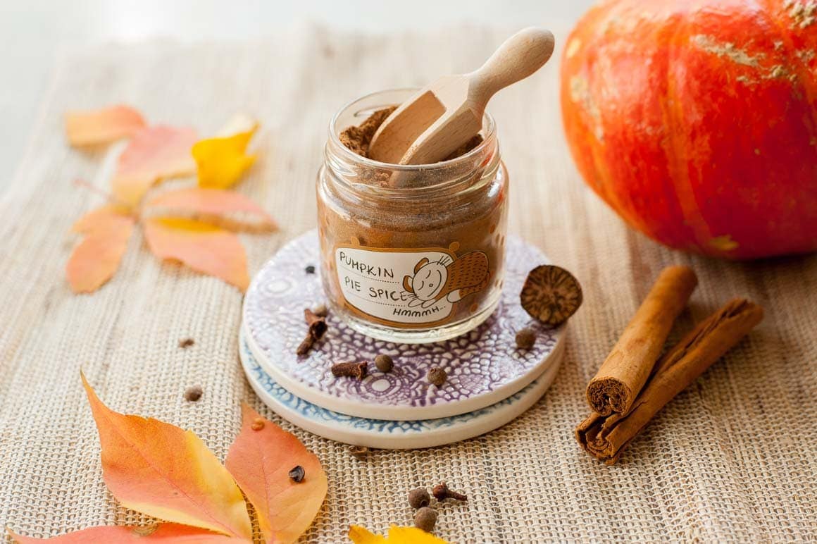 Pumpkin pie spice in a small jar, pumpkin, spices and fall leaves in the background.