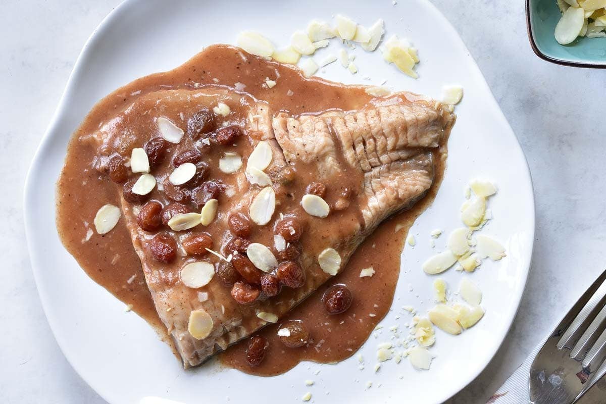 Carp with gingerbread sauce with almonds and raisins on a white plate.