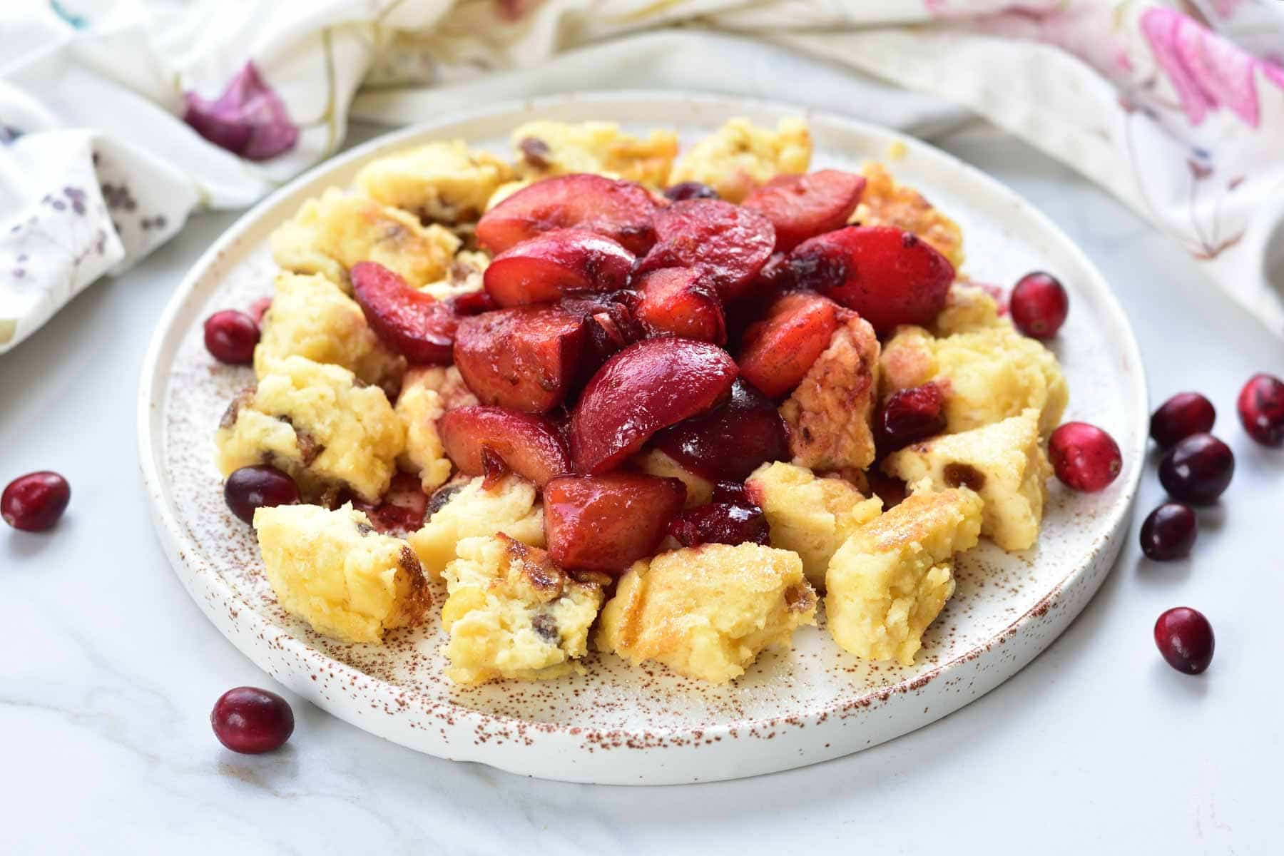Kaiserschmarrn topped with caramelized plum and cranberry sauce on a white plate.