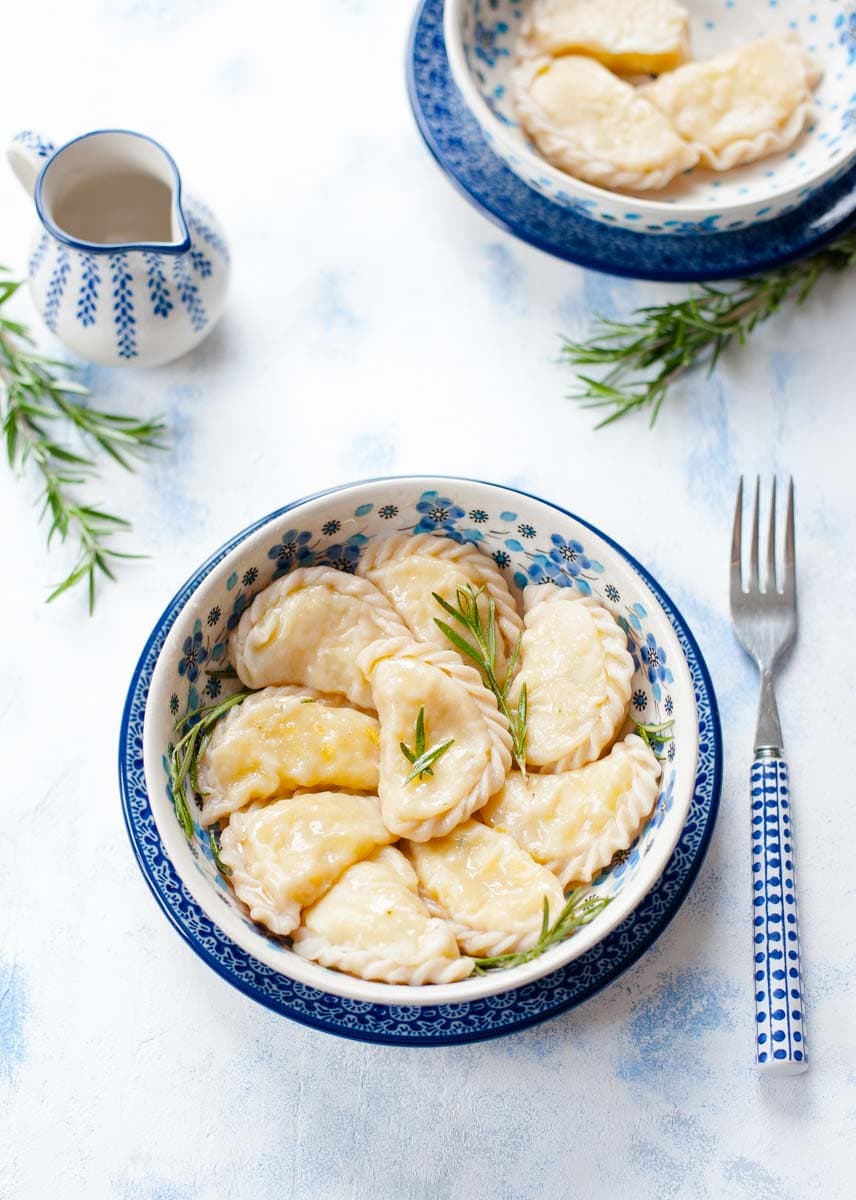 Potato and cheese pierogi with cheddar cheese in a blue bowl on a blue background.