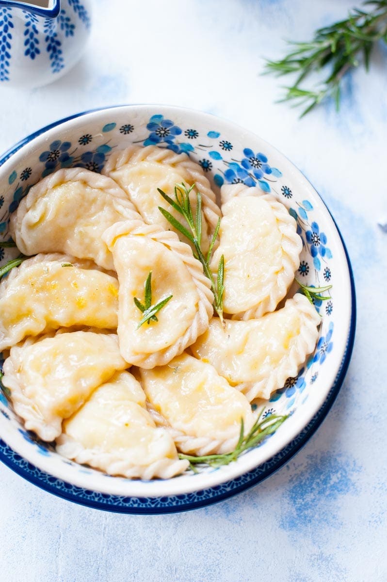 Potato and cheese pierogi in a blue bowl with rosemary twigs on top.