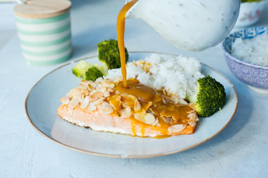 Orange ginger sauce is being poured over salmon with almonds.