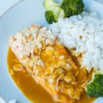 a piece of salmon covered in flaked almonds with orange ginger sauce, coconut rice and broccoli on a blue plate