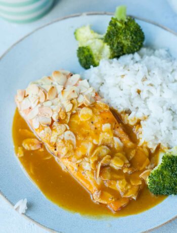a piece of salmon covered in flaked almonds with orange ginger sauce, coconut rice and broccoli on a blue plate