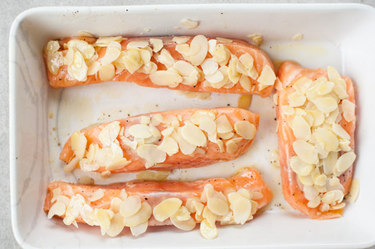 Salmon fillets covered with almond flaked in a baking dish.