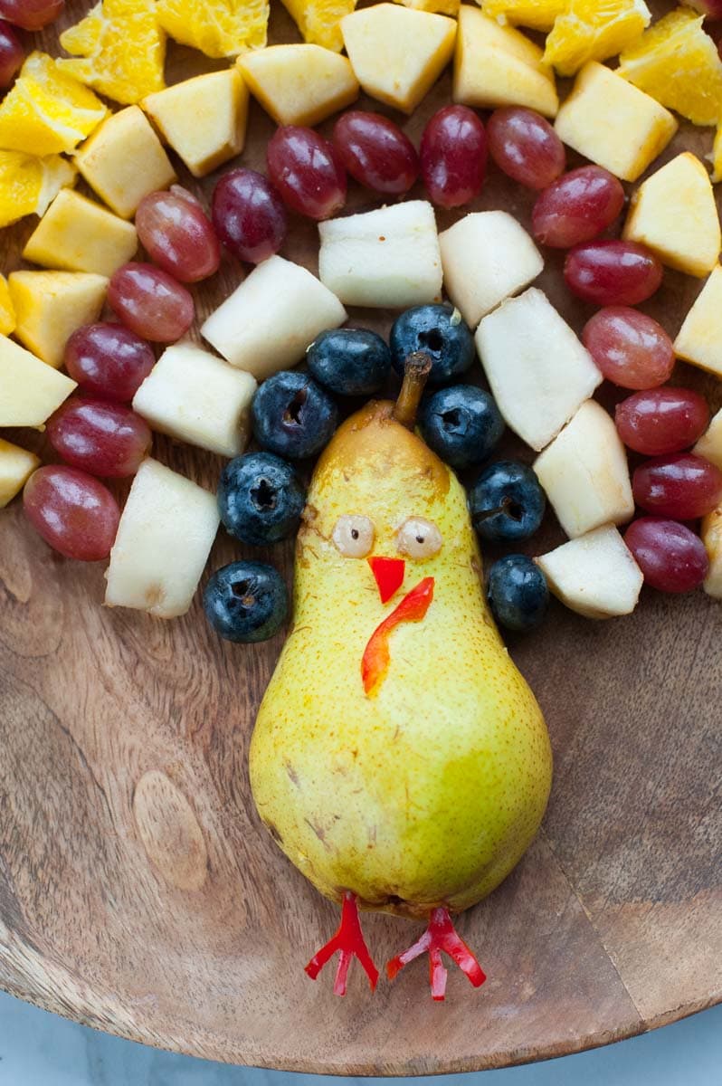 a close up shot on chopped fruits arranged in a shape of turkey on a wooden board