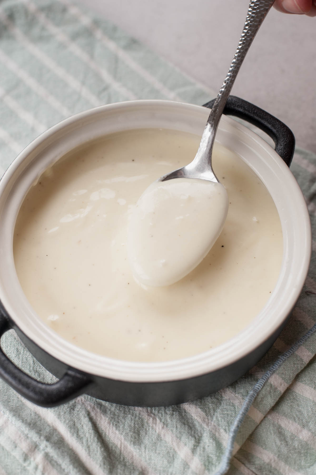 Bechamel sauce in a black pot is being spooned with a spoon.