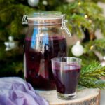 a big jar and a small glass filled with beet kvass, Christmass tree in the background