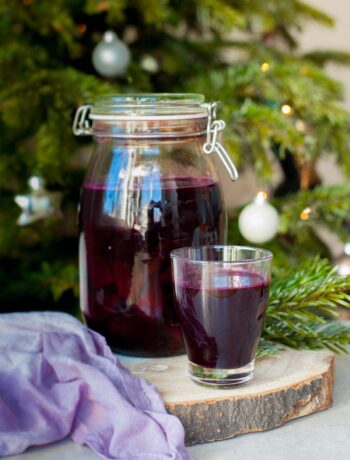a big jar and a small glass filled with beet kvass, Christmass tree in the background