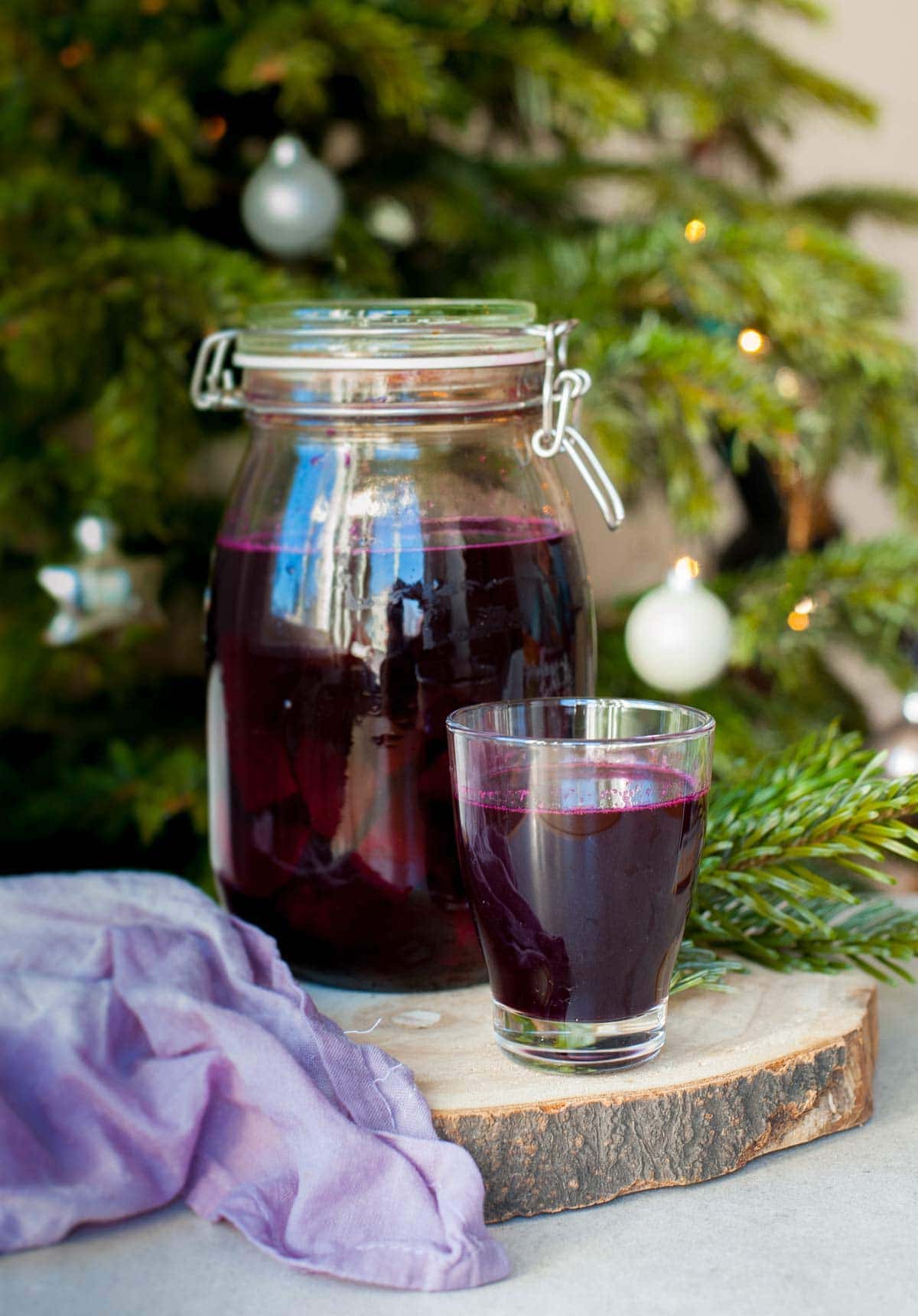 Beet kvass in a jar and a glass, Christmas tree in the background.