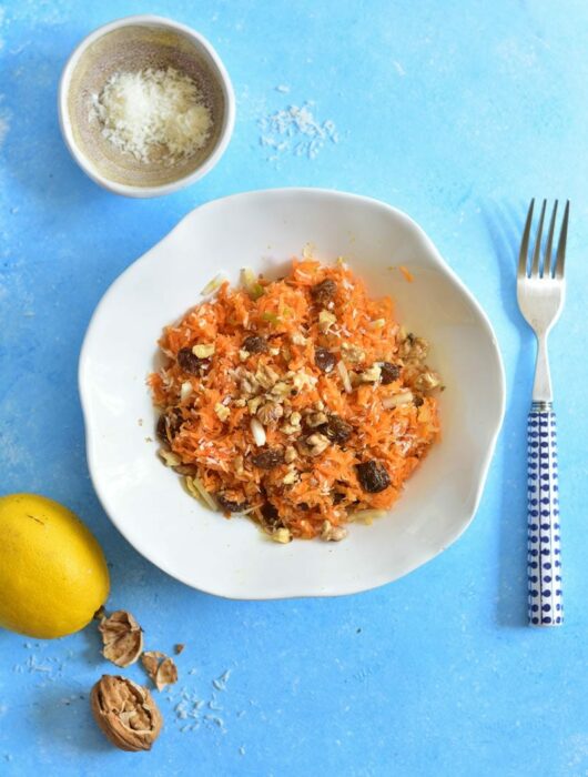 white plate with carrot apple salad on a blue background