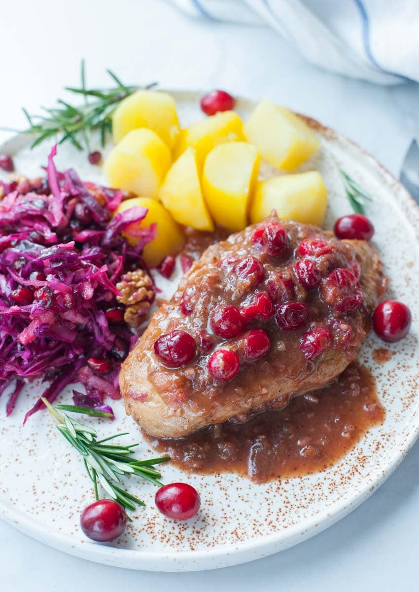 Cranberry balsamic chicken on a plate with cooked potatoes and red cabbage slaw.