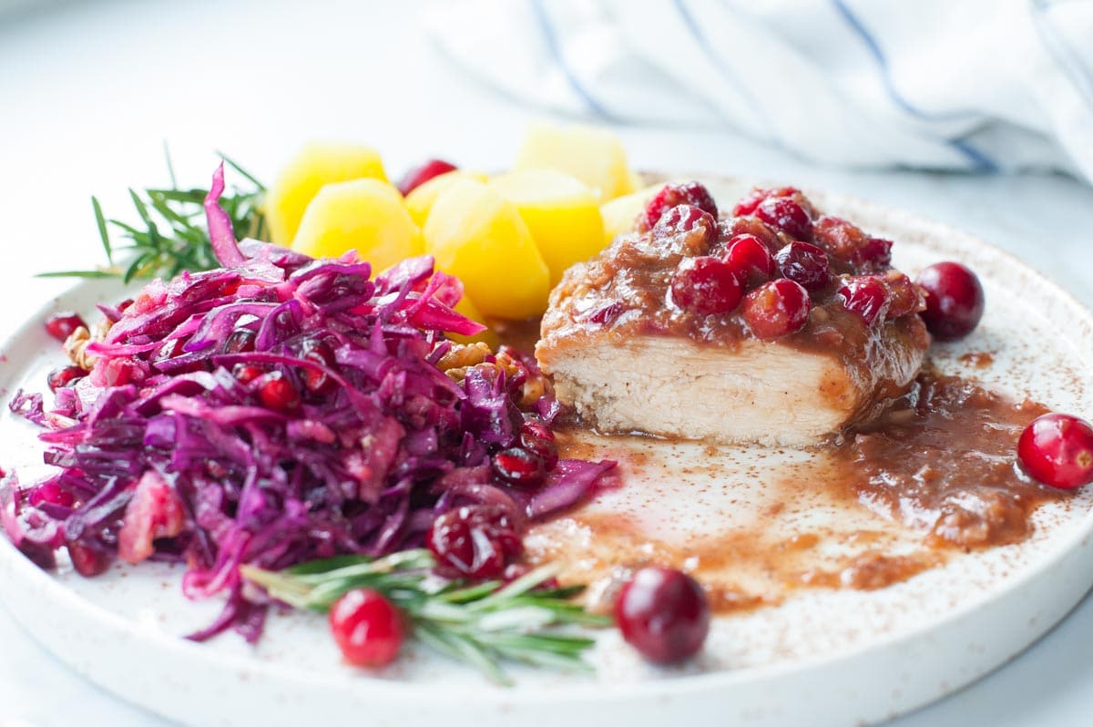 Cranberry balsamic chicken on a plate with cooked potatoes and red cabbage slaw.