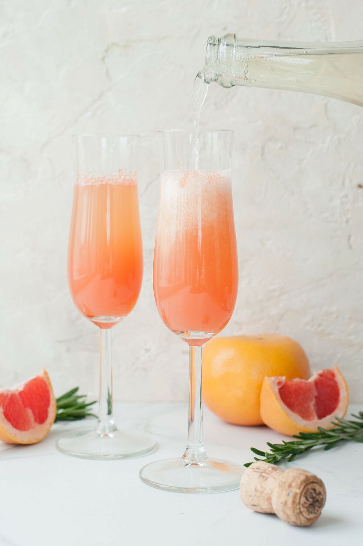 Champagne is being poured over grapefruit juice in a champagne glass.