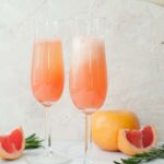 two champagne glasses filled with grapefruit mimosa