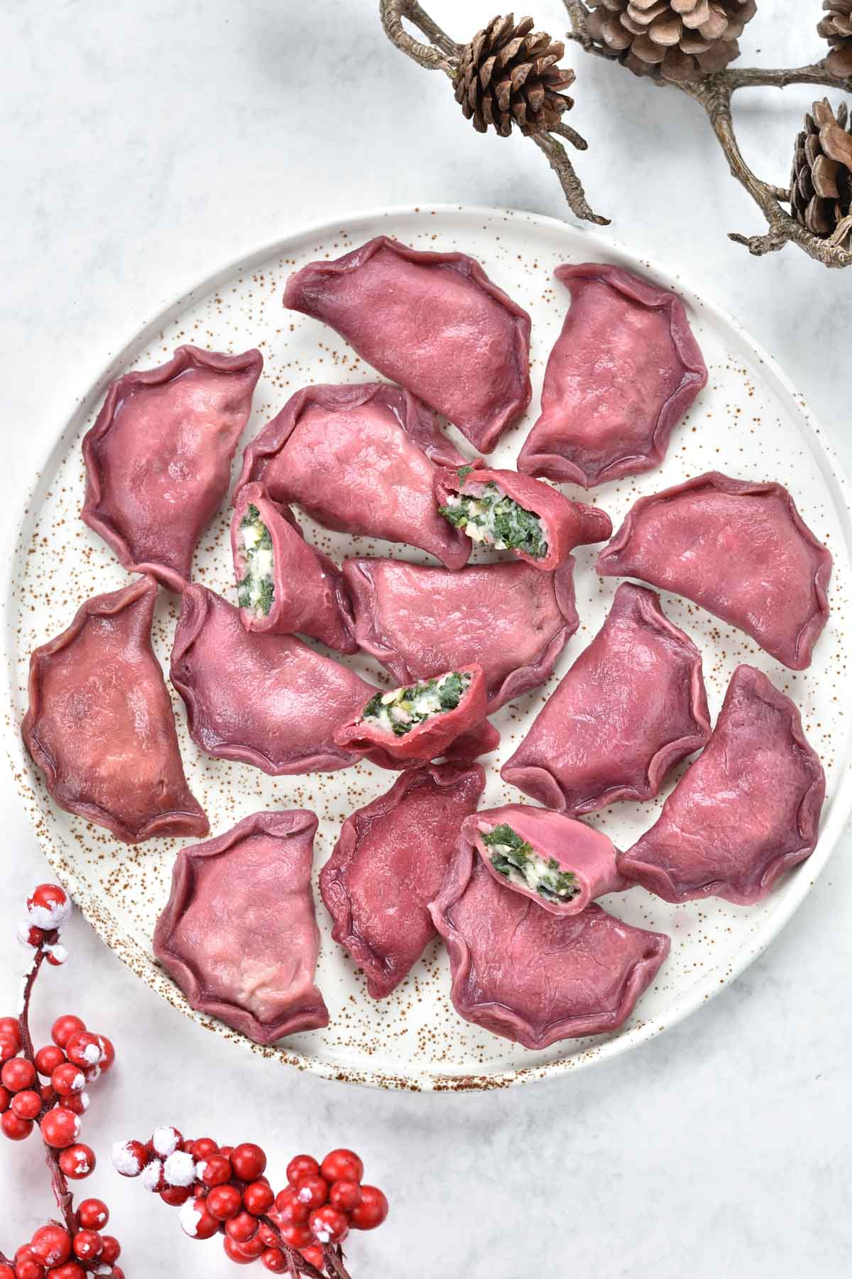Pink pierogi with spinach and potato filling on a white plate.
