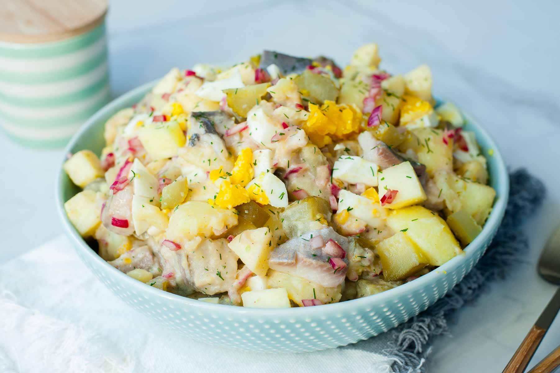 Herring salad with eggs, potatoes, and cucumbers in brine ib a green bowl.
