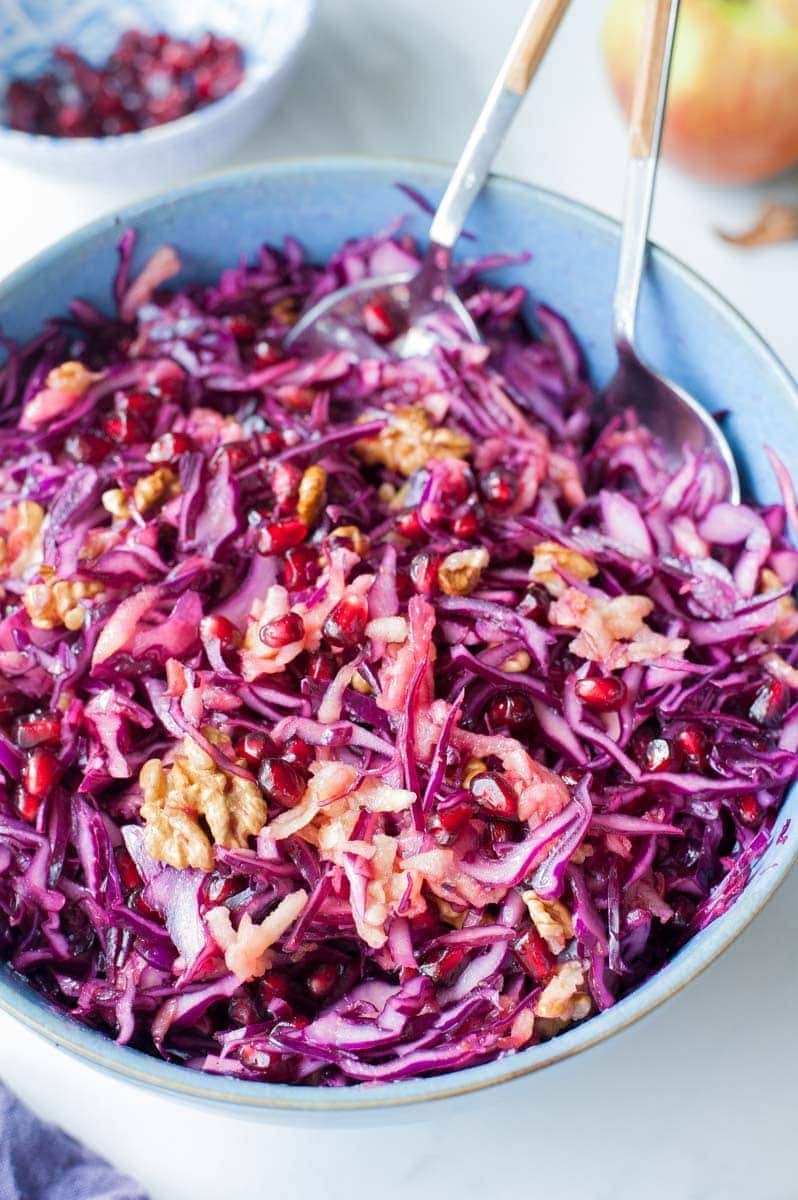 Close up picture of red cabbage apple slaw with pomegranate and walnuts in a blue bowl.