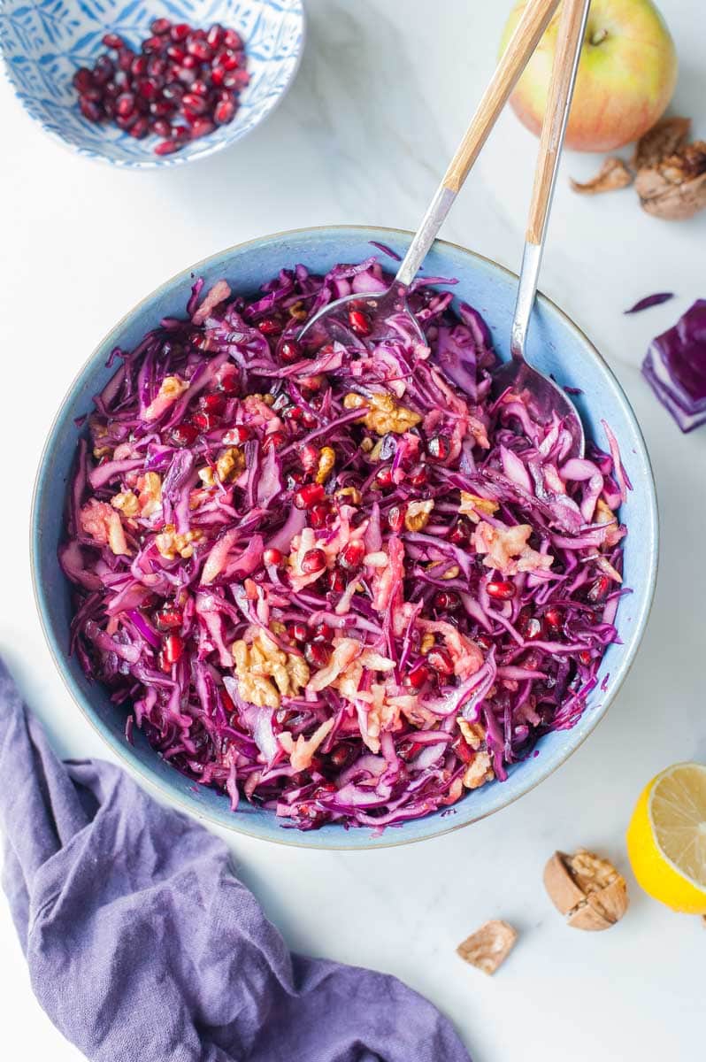 Red cabbage apple slaw with pomegranate and walnuts in a blue bowl.