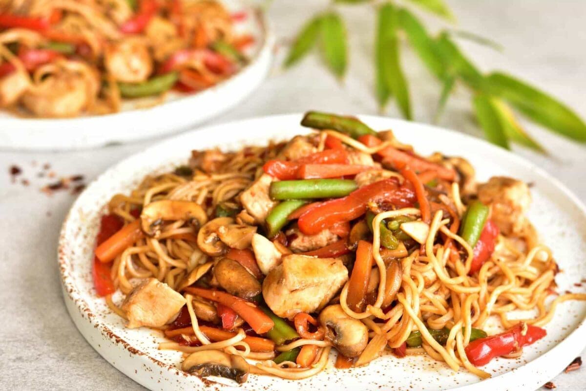 close up shot on sweet and sour chicken with noodles and vegetables on a white plate