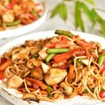 sweet and sour chicken with noodles and vegetables on a white plate
