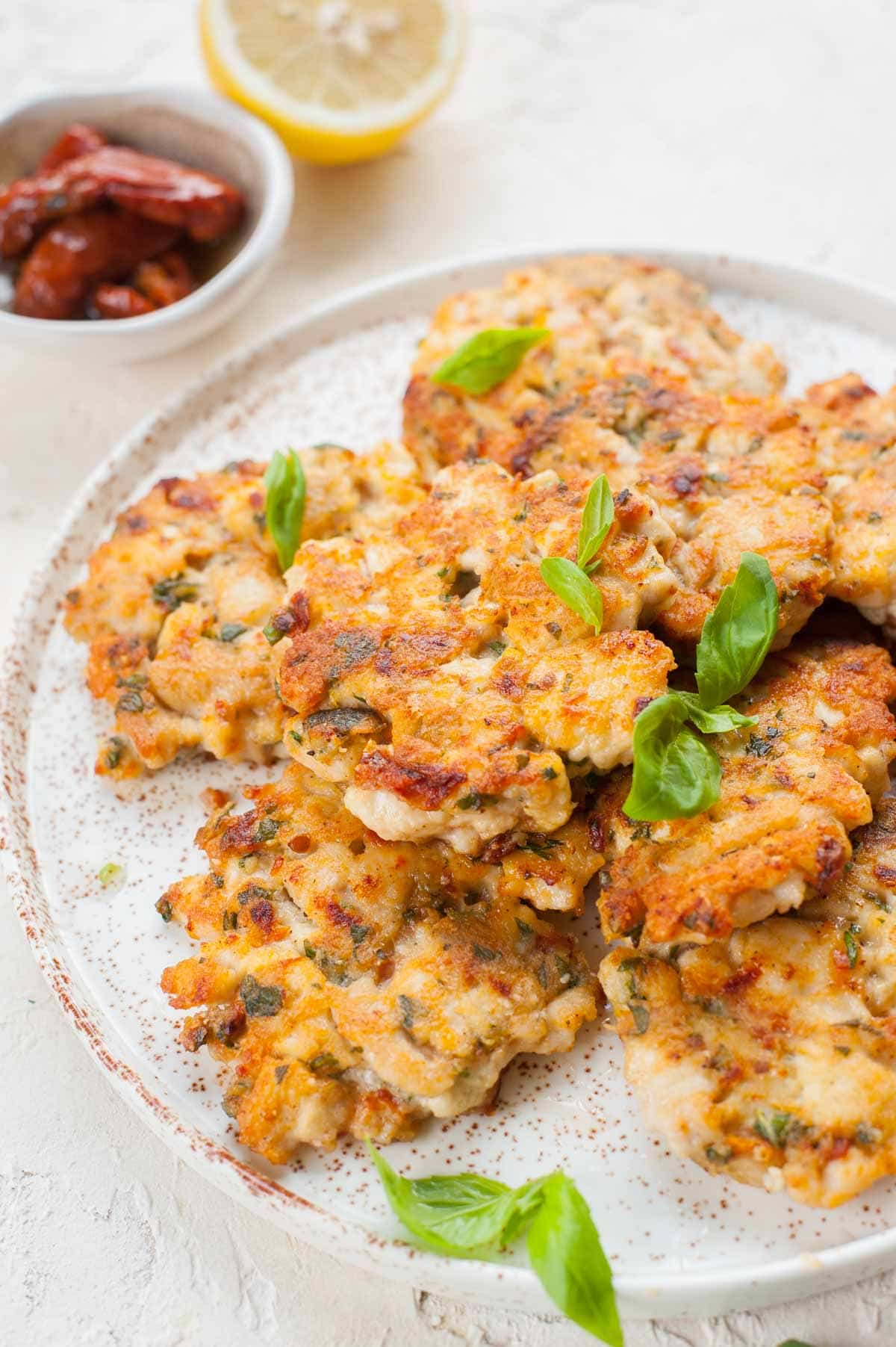 Chicken fritters with sun-dried tomatoes and basil on a white plate.