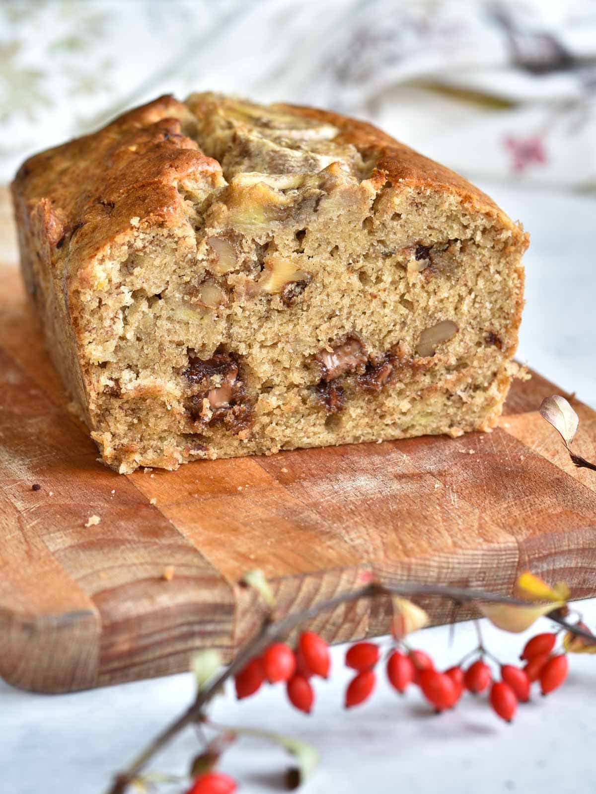 Banana bread with chocolate and nuts cut in half on a chopping board.