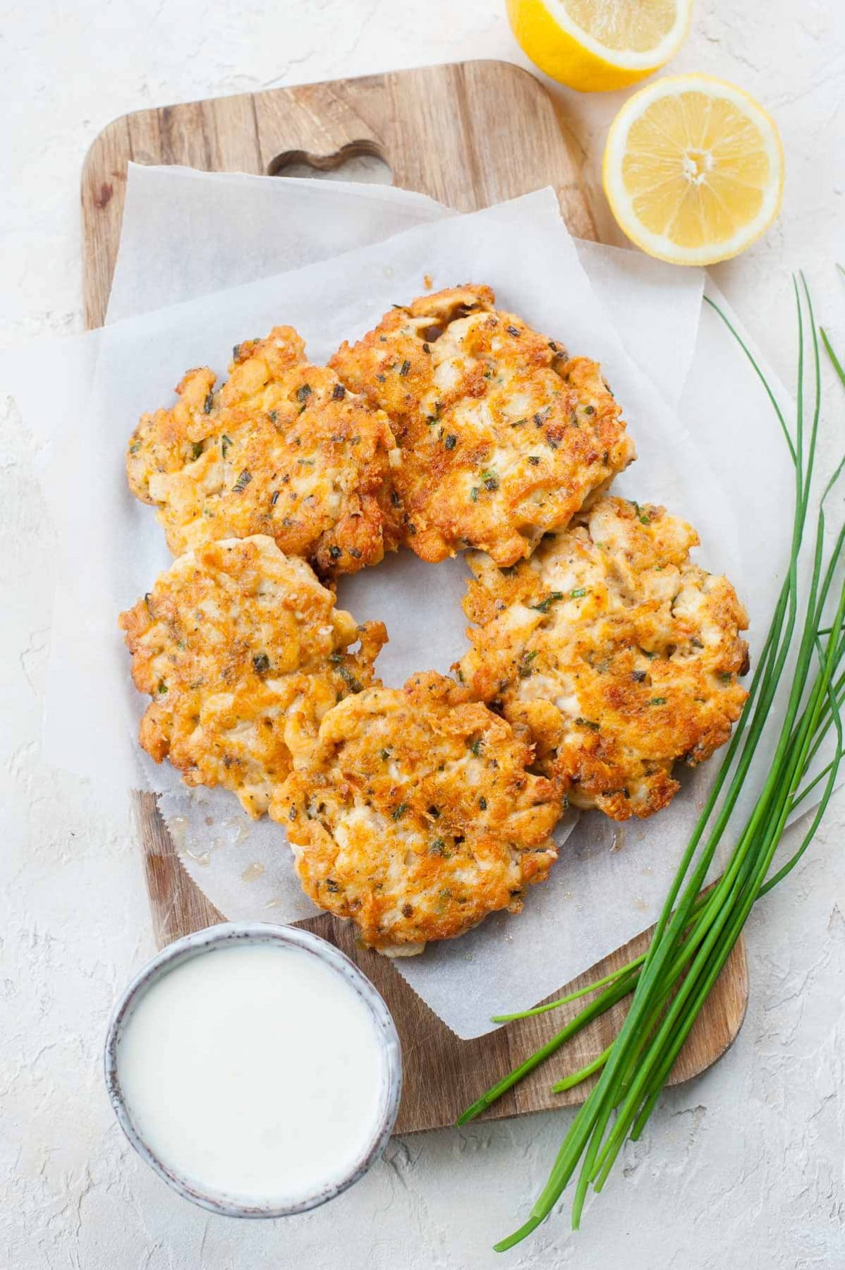 cheesy chicken fritters on a wooden board, surrounded with chives and lemon halves