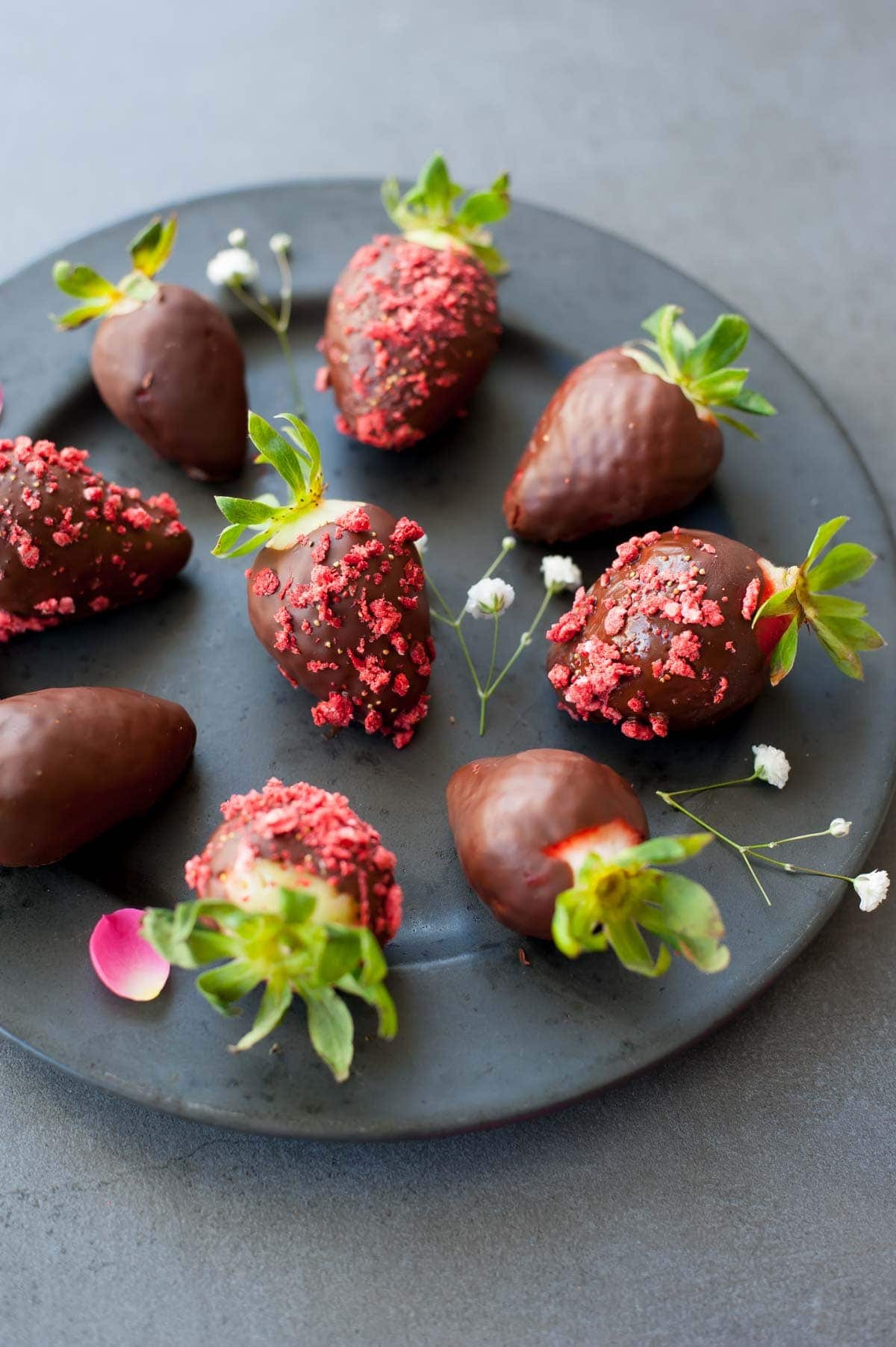 Chocolate covered strawberries on a black plate.