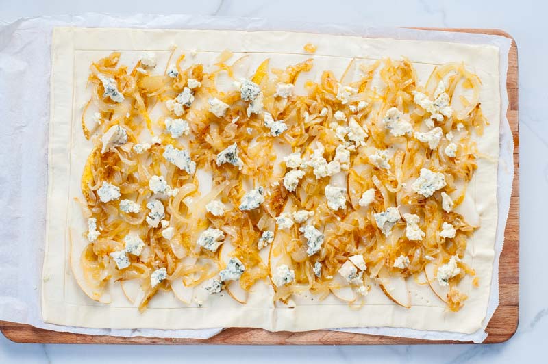 raw puff pastry topped with caramelized onions, pear slices and blue cheese