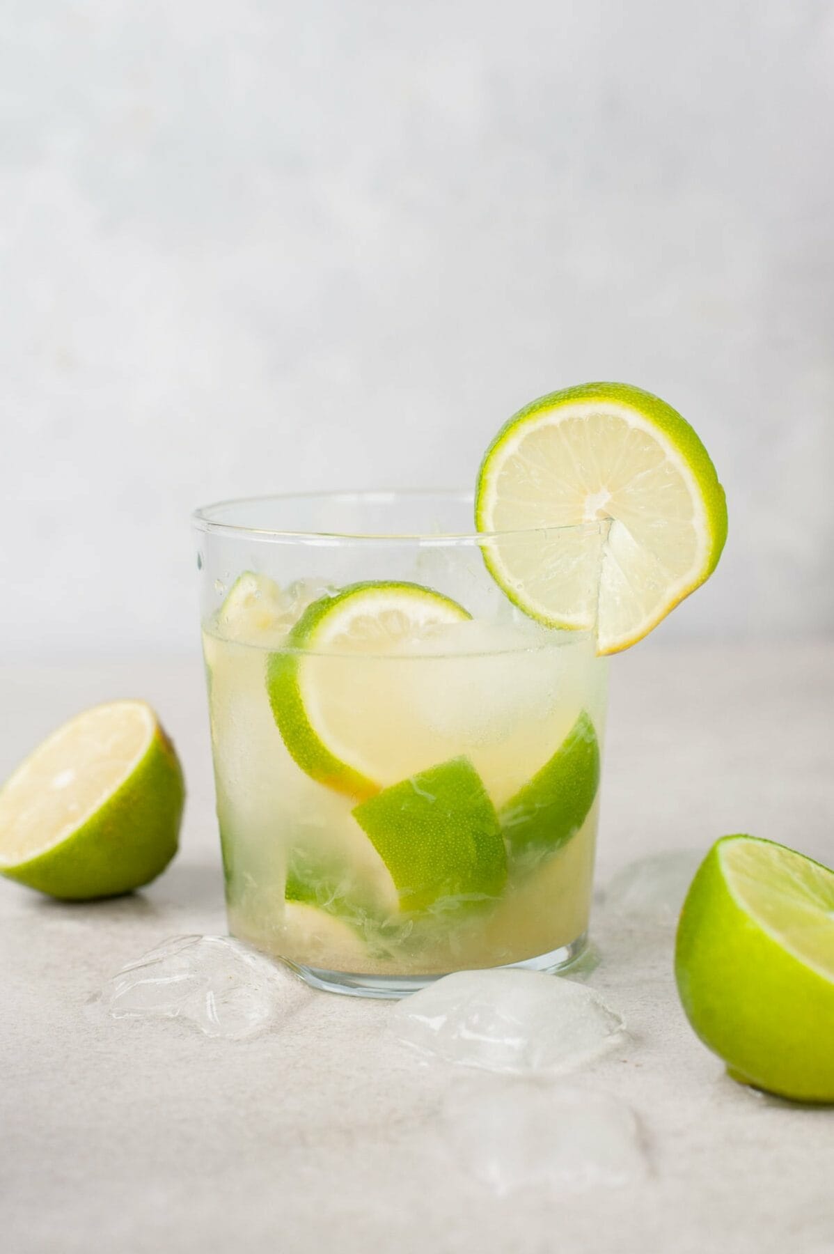 A small glass with caipirinha- Limes and ice around the glass.