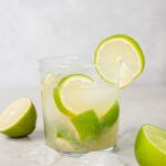 caipirinha in a glass, ice cubes and limes in the background