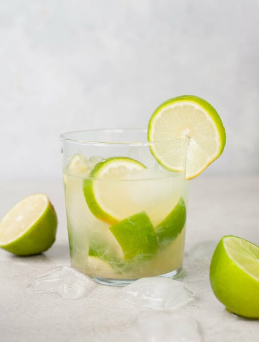 caipirinha in a glass, ice cubes and limes in the background