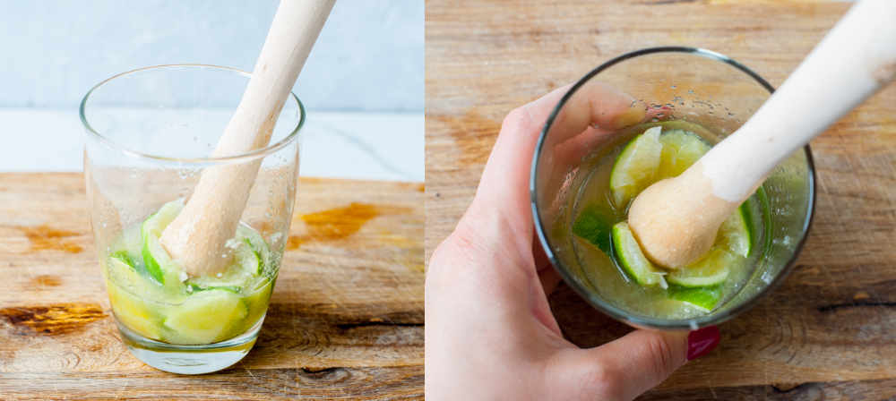 Limes and sugar are being mashed with a muddles in a glass.