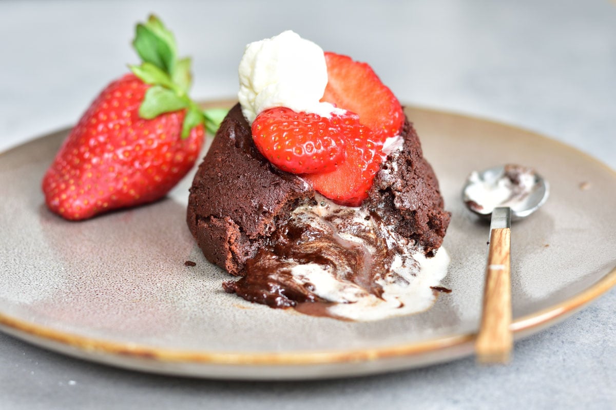 Chocolate lava cake on a plate with strawberries and whipped cream.