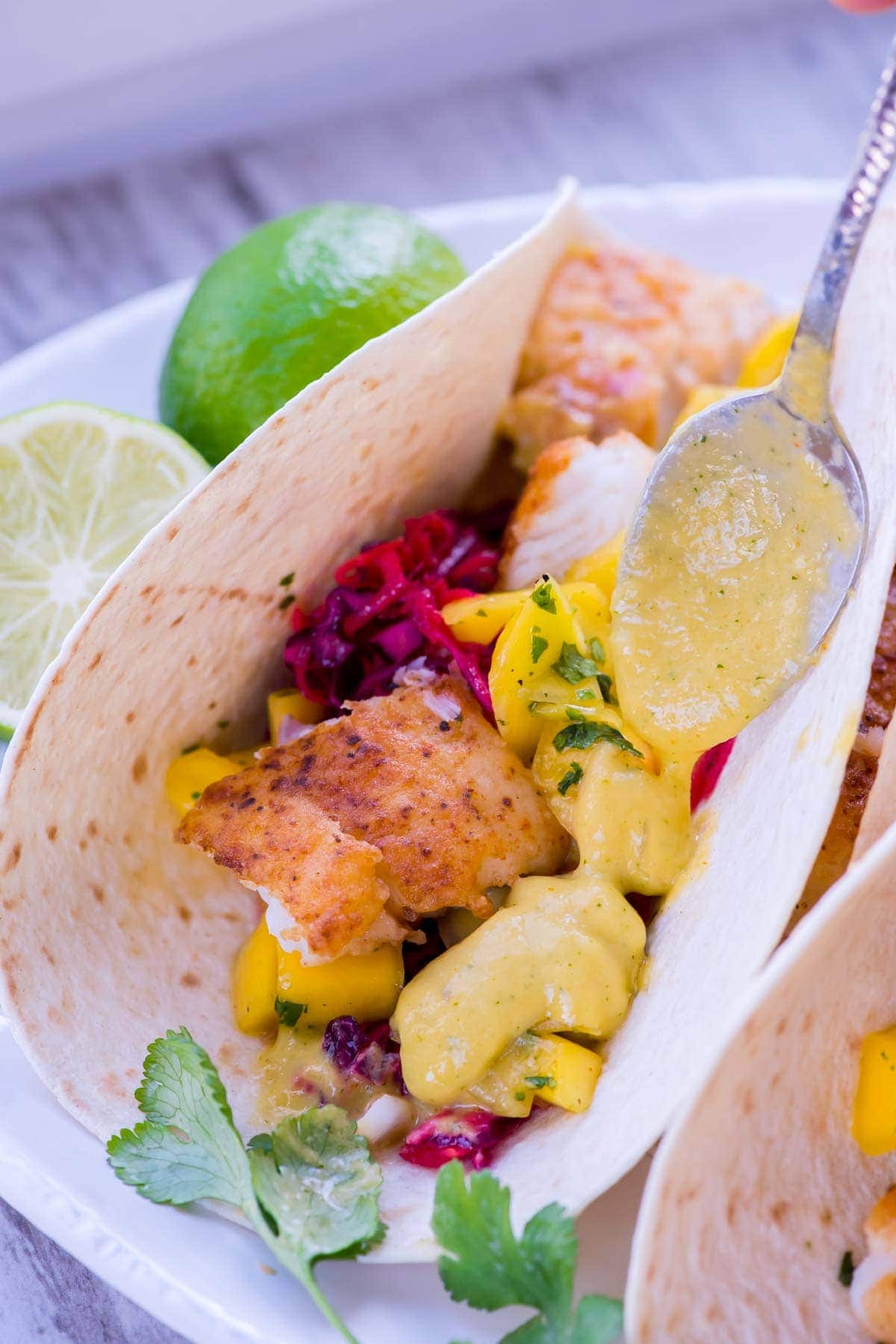 Mango sauce is being spooned over a fish taco.