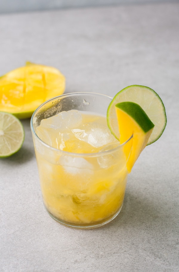 Mango caipirinha in a glass. Mango fruit and lime in the background.